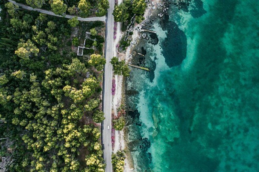 A coastal road with dense greenery and clear turquoise waters. 3