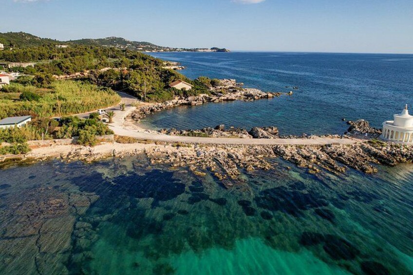 A coastal landscape with clear turquoise waters, rocky shorelines, and a white building near the water's edge. 5