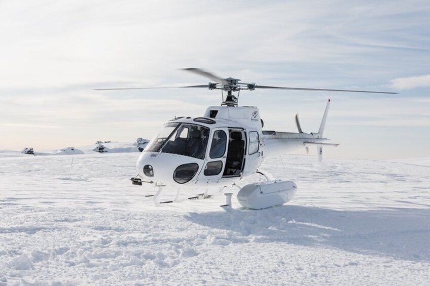 A white helicopter with a snow-covered landing area and a small aircraft in the background. 4