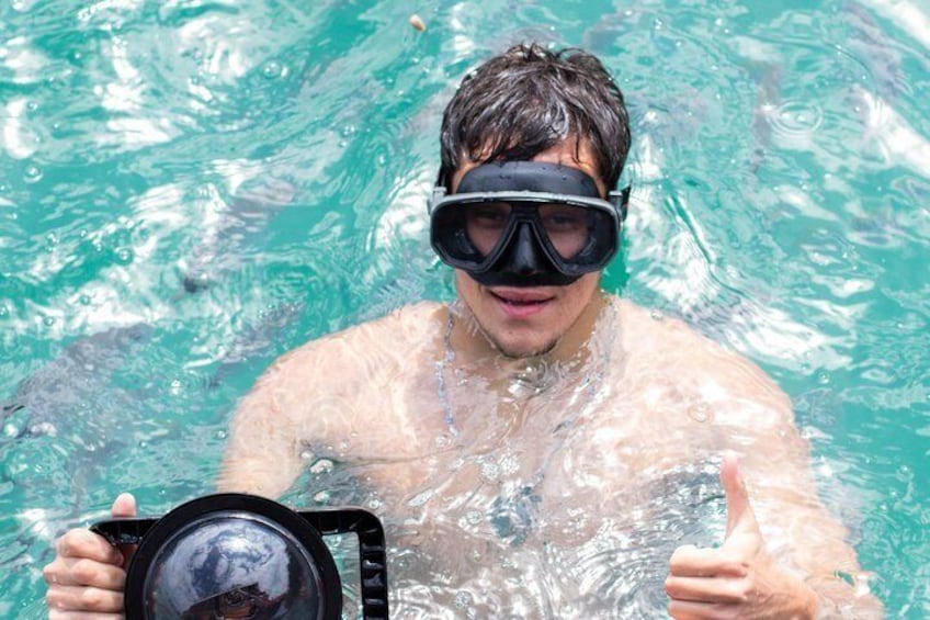 A person swimming in clear water, holding a camera, and giving a thumbs-up. 5