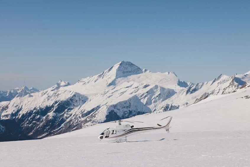 A snow-covered mountain range with a helicopter on the ground. 1