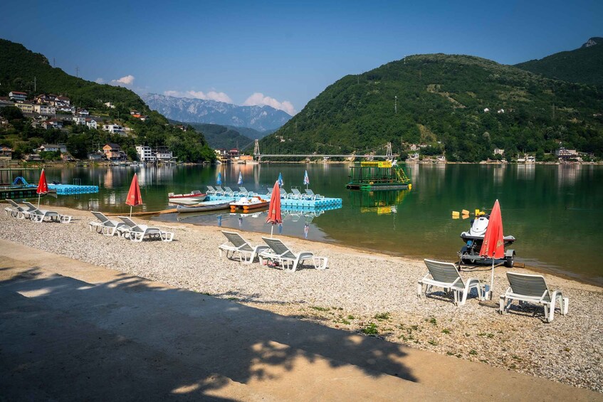 A lakeside beach with lounge chairs and umbrellas, boats, and a bridge in the background. 3