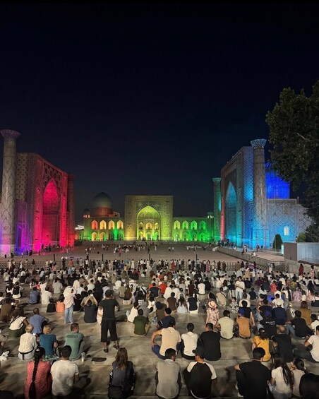 A large crowd gathered in front of a brightly lit building with intricate architectural details. 2