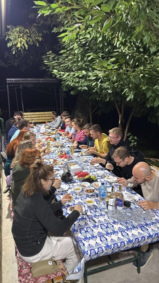 A group of people dining outdoors at night with a table covered in a patterned tablecloth. 3