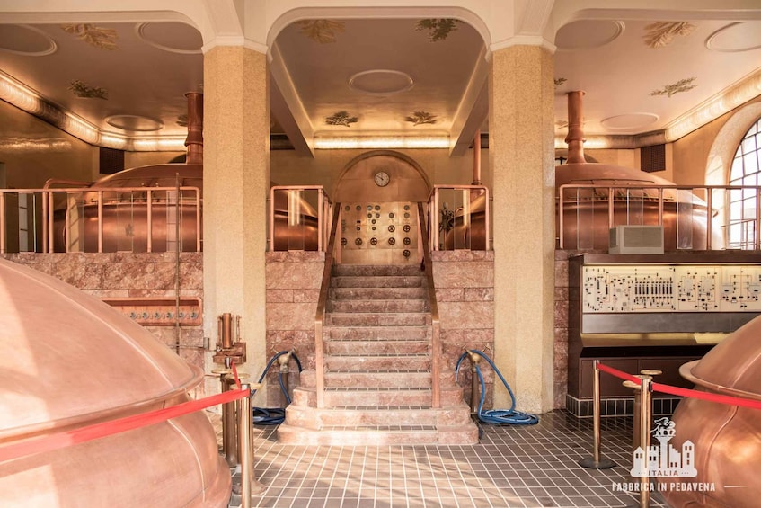 A historic industrial building with large copper vats, a central staircase, and a control panel. 4