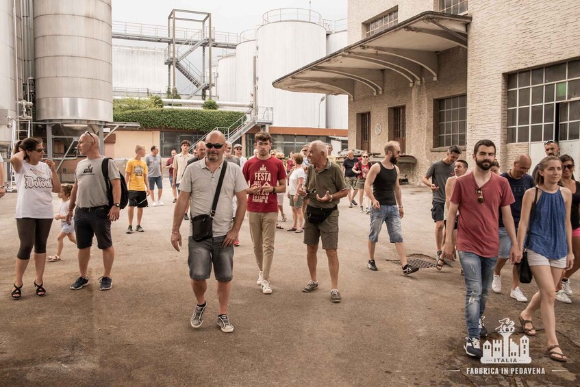 A group of people walking in an industrial area with buildings and large tanks in the background. 5