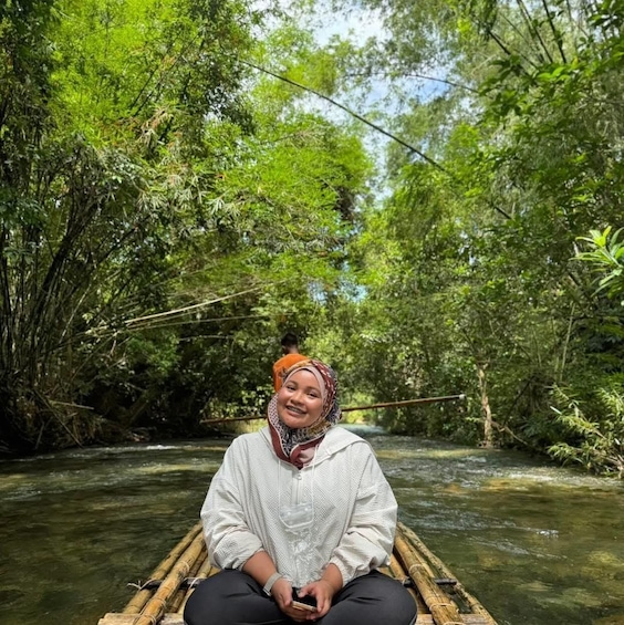 A person sitting on a bamboo raft in a river surrounded by dense green foliage. 5