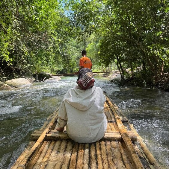 A person sitting on a bamboo raft in a river surrounded by dense green foliage. 4