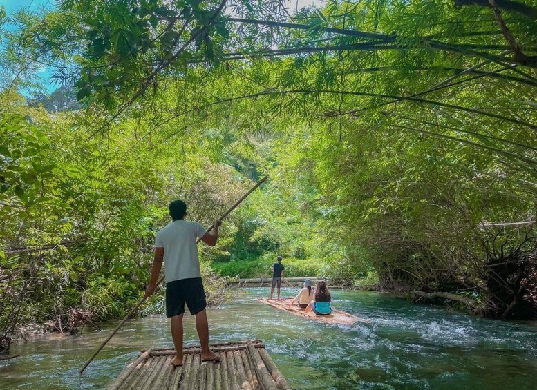 A river with people on a bamboo raft, surrounded by dense green foliage. 1