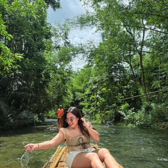 A person sitting on a bamboo raft in a river surrounded by dense green foliage. 2
