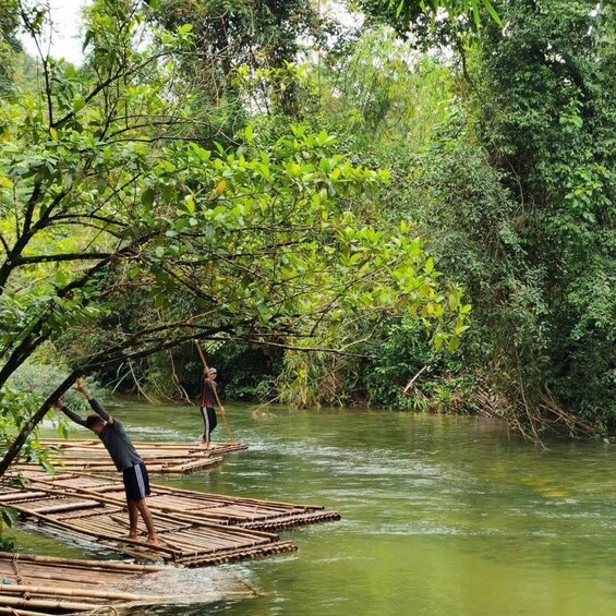 Two people walking on bamboo rafts in a river surrounded by dense greenery. 3