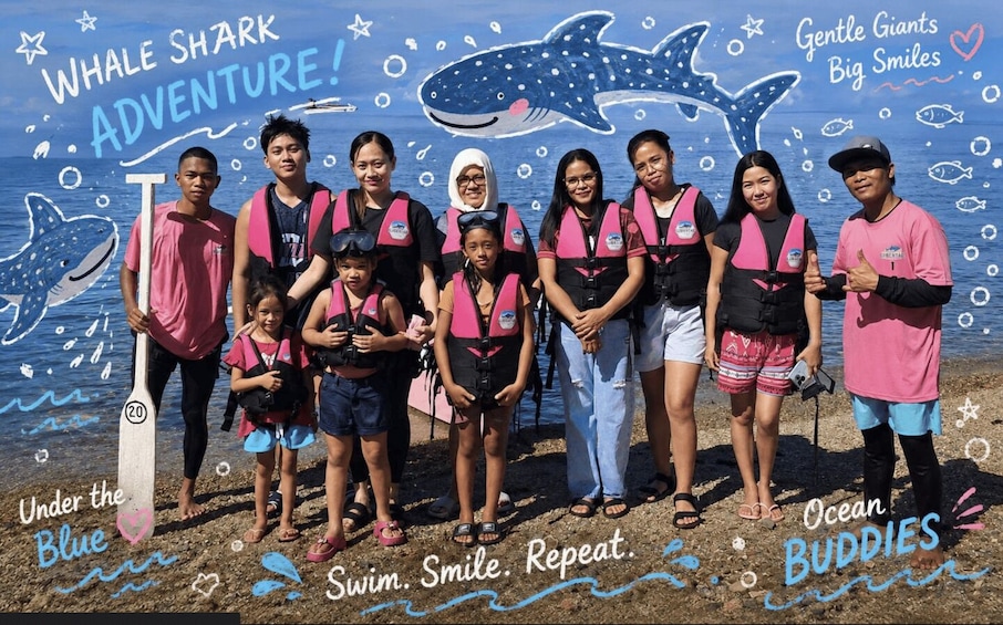 A group of people at a beach with a whale shark adventure theme, wearing life vests and standing in front of a mural with a whale shark and ocean-related drawings. 5
