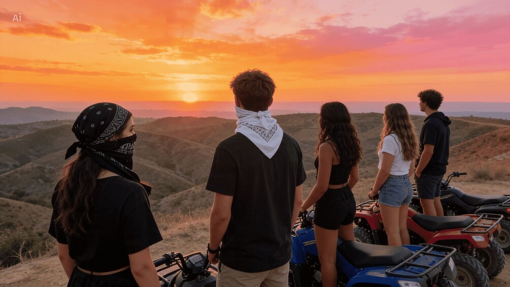 A group of people standing on a hill overlooking a sunset with a mountainous landscape in the background. 4