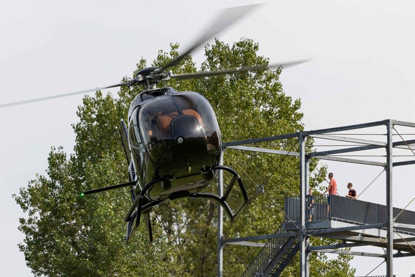 A black helicopter hovering above a metal structure with people on a platform. 4