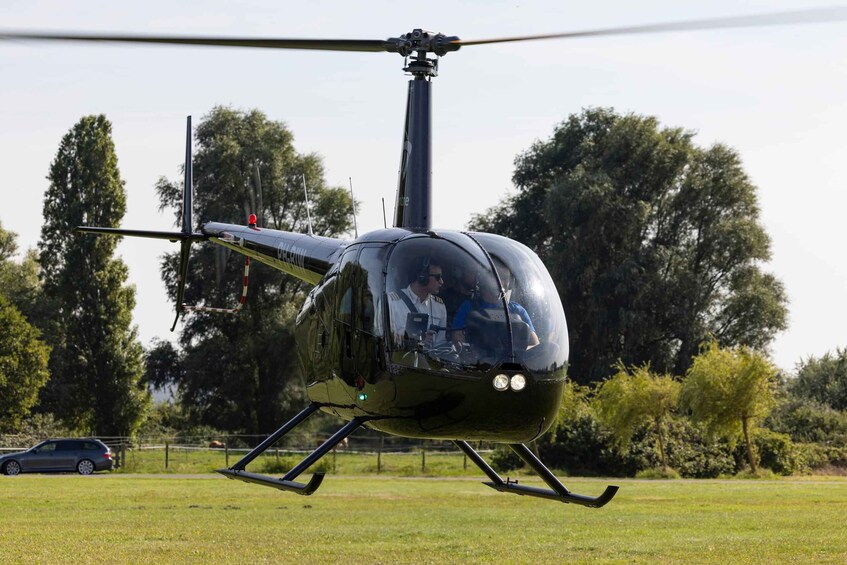 A helicopter hovering over a grassy field with trees in the background. 3