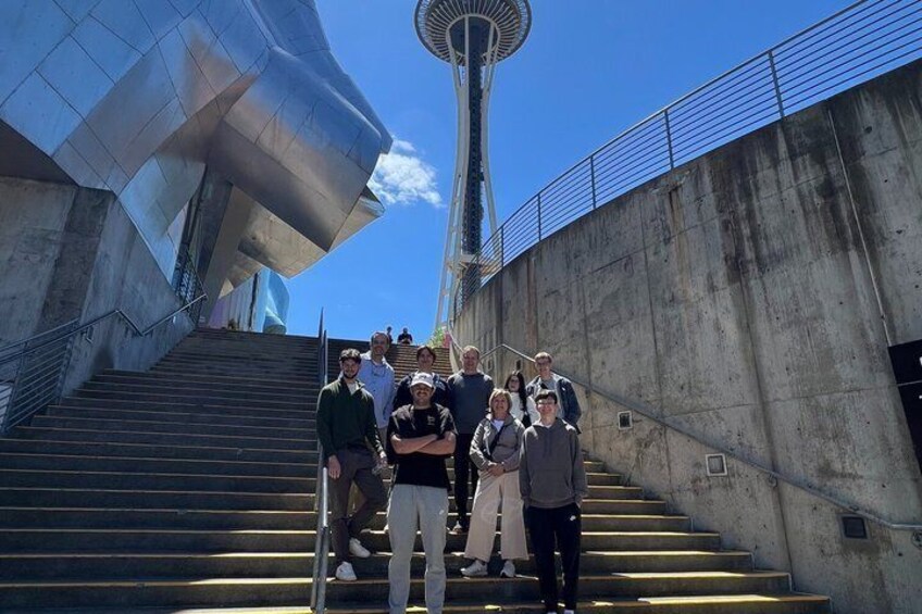 A group of people standing on a staircase with a futuristic building and a tower in the background. 1