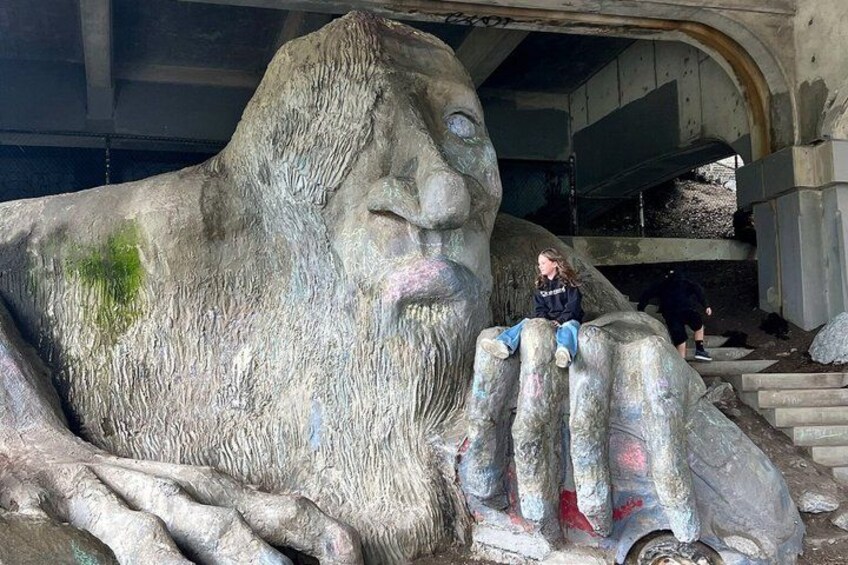 A large rock sculpture with a face and hands, a person sitting on the sculpture, and a staircase leading up to it. 5