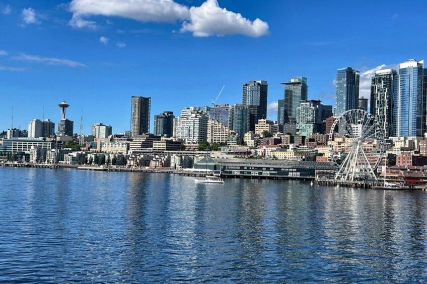 A city skyline with modern buildings, a Ferris wheel, and a body of water reflecting the city. 3