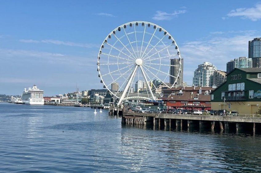 A waterfront cityscape with a large Ferris wheel, a cruise ship, and modern buildings. 3