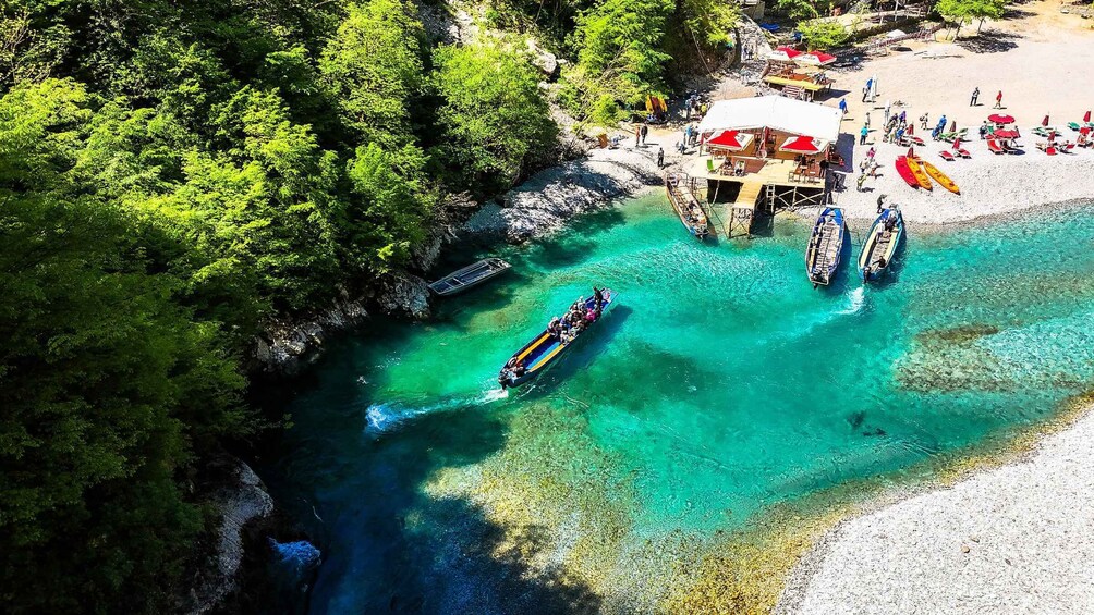 A river with clear turquoise water, surrounded by dense green forest, and a beach with umbrellas and boats. 5