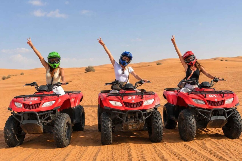 Three people on red ATVs in a desert with sand dunes in the background. 1