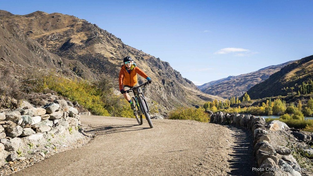 A person riding a mountain bike on a dirt path surrounded by rocky terrain and sparse vegetation. 1