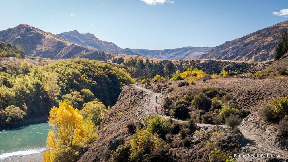 A mountainous landscape with a river, autumn-colored trees, and a dirt path. 4