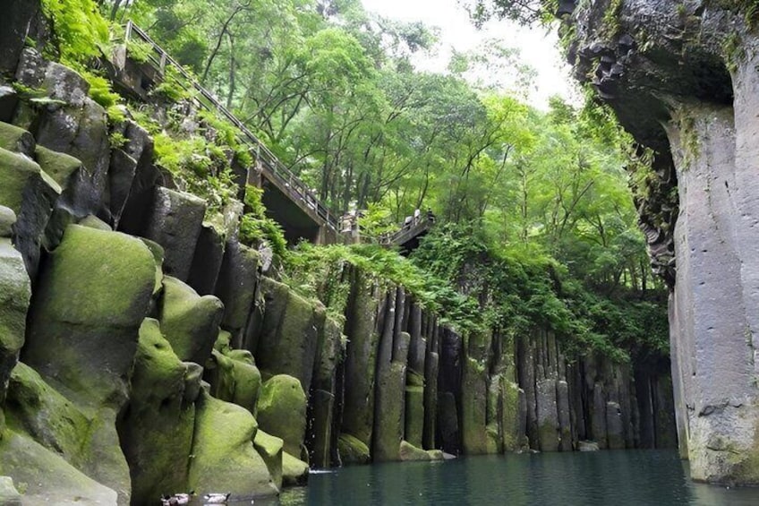 A forested area with a water body, rocky formations, and a wooden bridge. 2