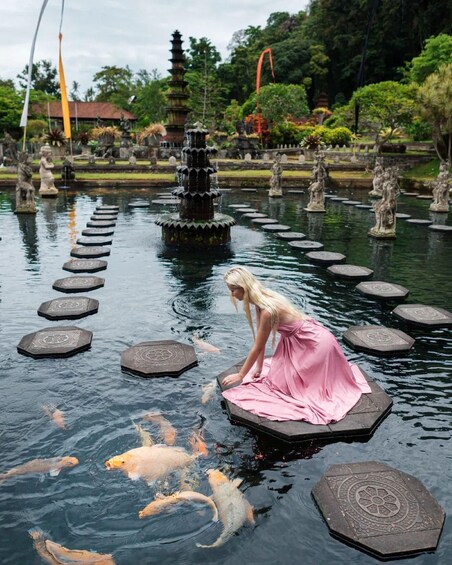 A woman in a pink dress feeding koi fish in a pond with stepping stones and a pagoda in the background. 4