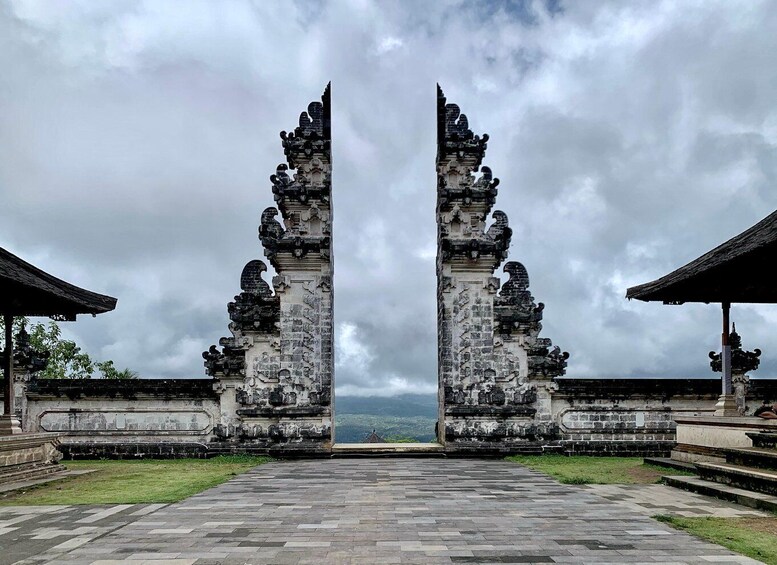 A temple entrance with two ornate stone pillars and a view of the landscape beyond. 3