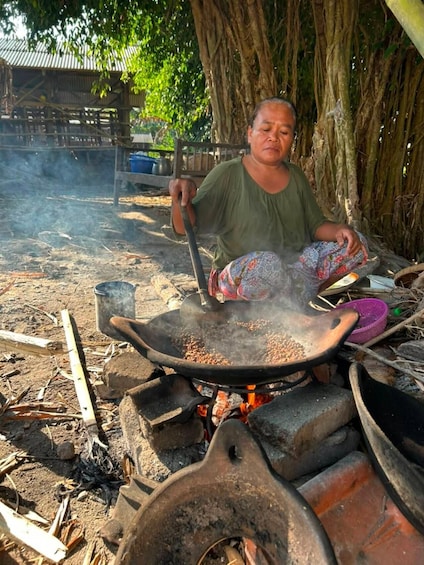 A person cooking outdoors using a large pan over an open fire. 1