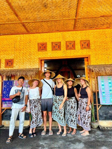 A group of people standing in front of a traditional thatched-roof building with decorative wooden carvings. 5