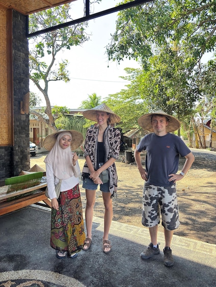 Three people standing outdoors, one wearing a traditional conical hat, another in casual attire, and the third in a t-shirt and shorts. 3
