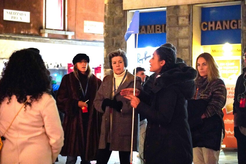 A group of people standing outdoors at night, with signs for 'SALIZZADA' and 'AMBIBI' visible in the background. 2