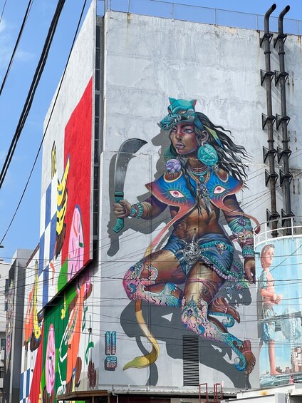 A large mural on a building featuring a colorful figure with a snake, a shield, and a bow. 3