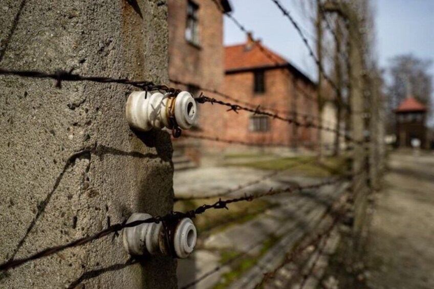 A barbed wire fence, a concrete wall, and a building with a red roof in the background. 4