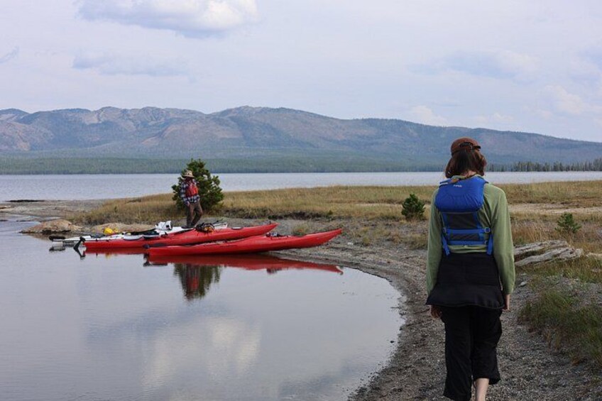 A person standing by a lake with a red kayak and a tree in the background. 2