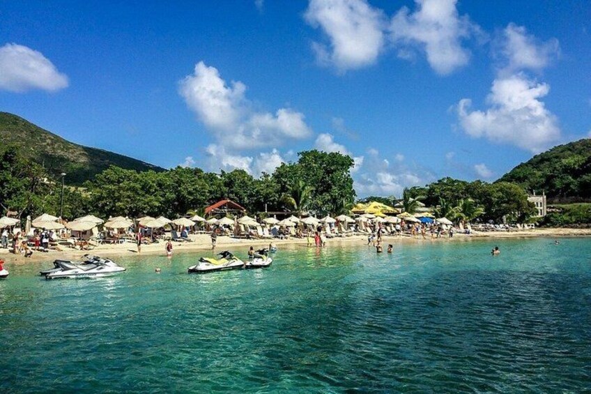A beach with clear turquoise water, umbrellas, and boats. 1
