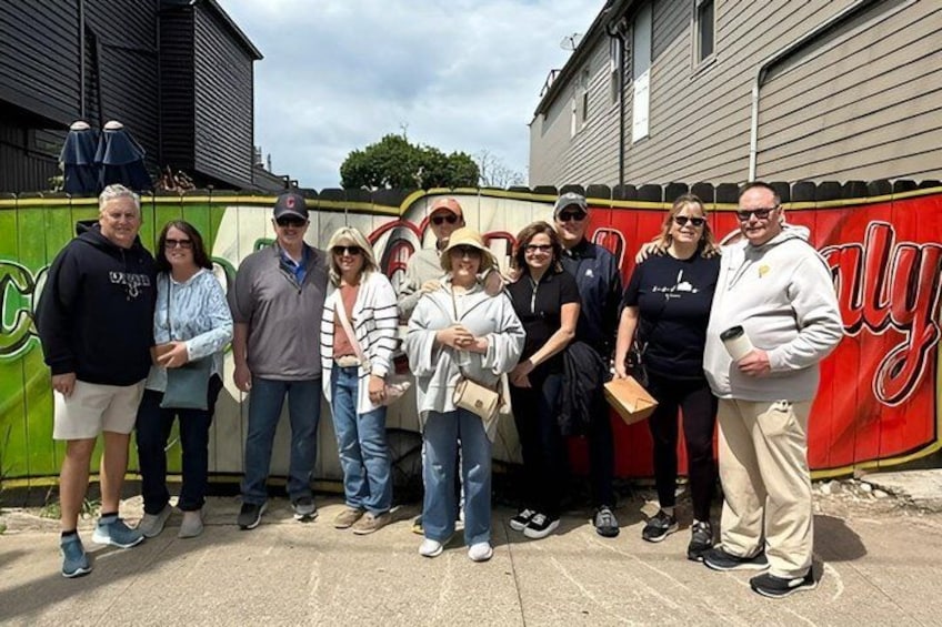 A group of people standing in front of a building with a red and green sign. 1