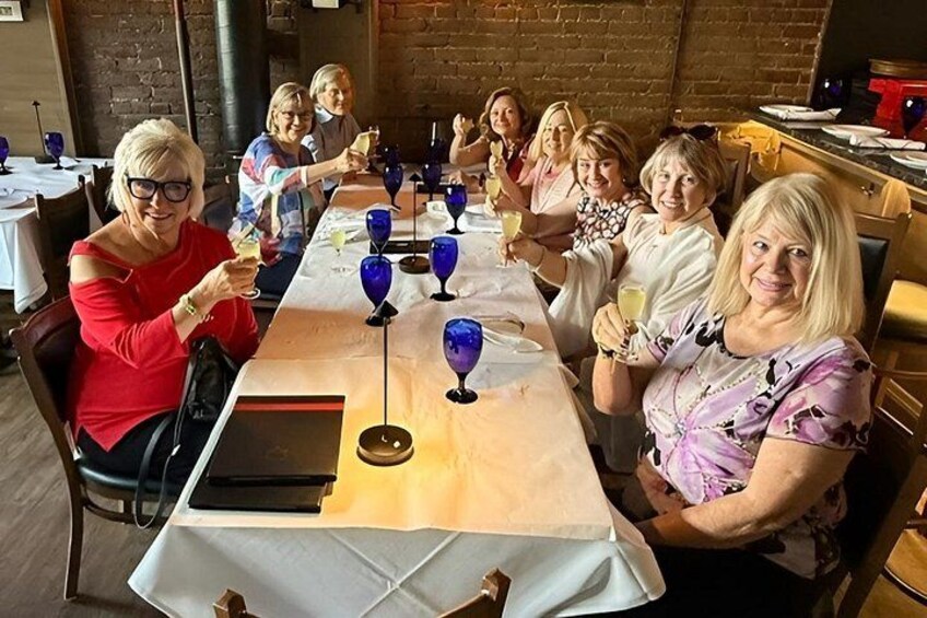 A group of people seated at a long table with wine glasses and a menu. 2