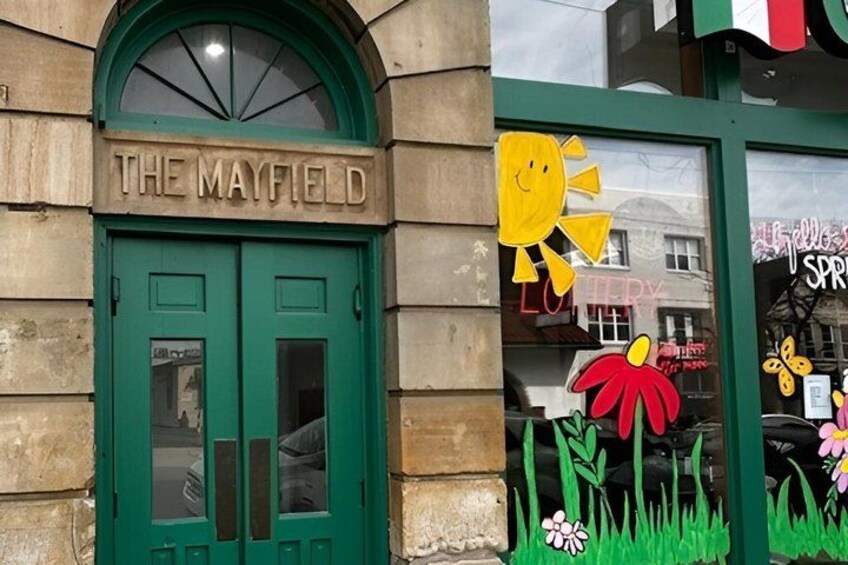 A building with a green door labeled 'THE MAYFIELD' and a window decorated with a sun and flowers. 4