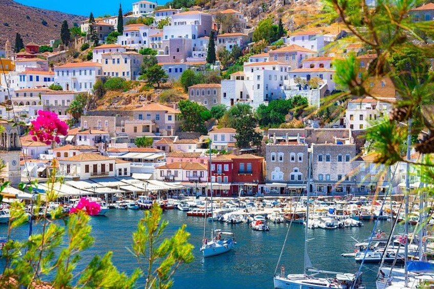 A coastal town with white buildings, a marina with boats, and a hillside with trees. 1