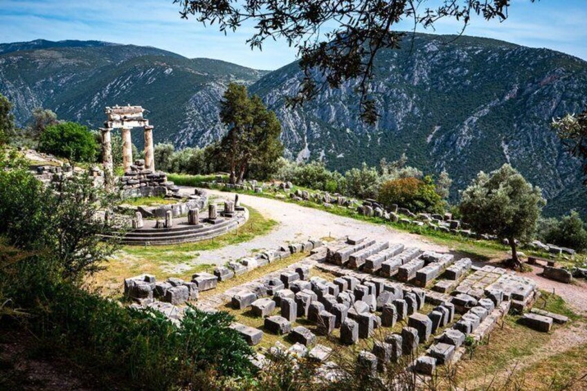 Ancient ruins with columns and stone blocks, surrounded by mountains and trees. 1