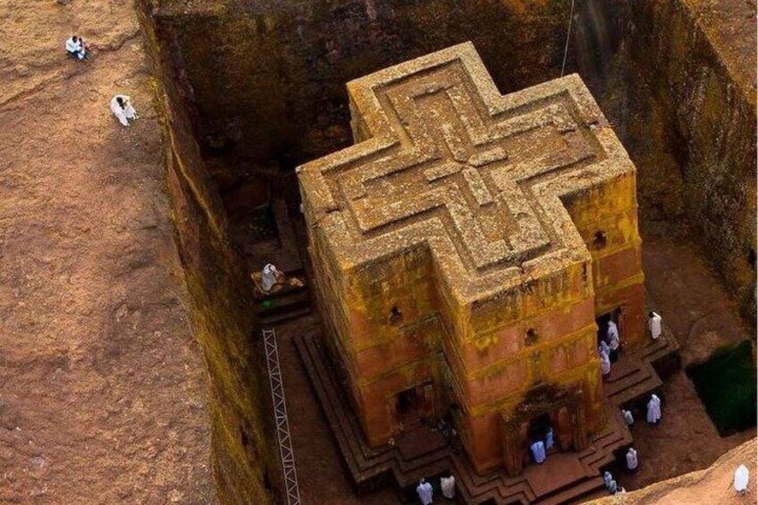 A large, ancient, multi-tiered stone structure with a cross-like pattern on top, situated in a deep, rocky excavation. 3