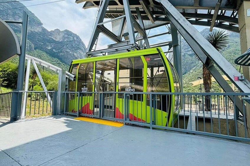 A green cable car with 'NUEVO' written on it, a metal staircase, and a mountainous landscape in the background. 3