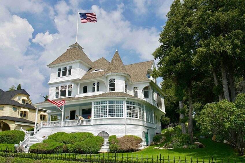 A large white house with a wrap-around porch, a flag, and a well-maintained garden. 4