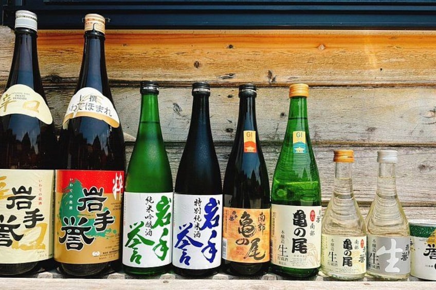 A row of variously shaped and colored bottles with Japanese labels, displayed against a wooden background. 2