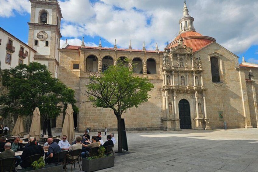 A plaza with outdoor seating, a historic building with a clock tower, and a tree in the center. 2