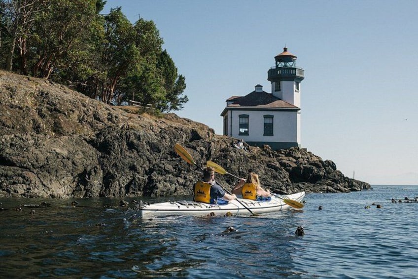A kayak on calm water near a rocky shore with a lighthouse in the background. 1