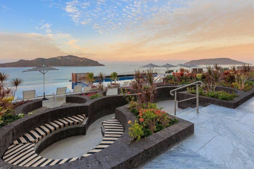 A landscaped outdoor area with a pool, lounge chairs, and a view of the sea. 5